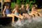 Kinder sitzen in einer Reihe am Rand eines Wasserbeckens. Sie spritzen das Wasser mit dem Füßen.